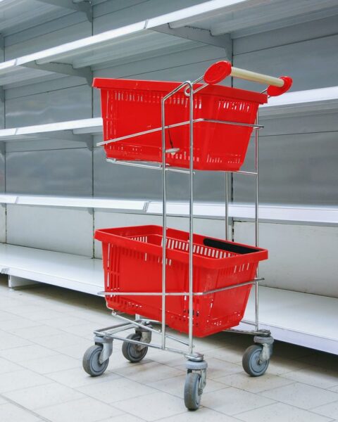 Shopping trolley with empty baskets against empty shelves in grocery store